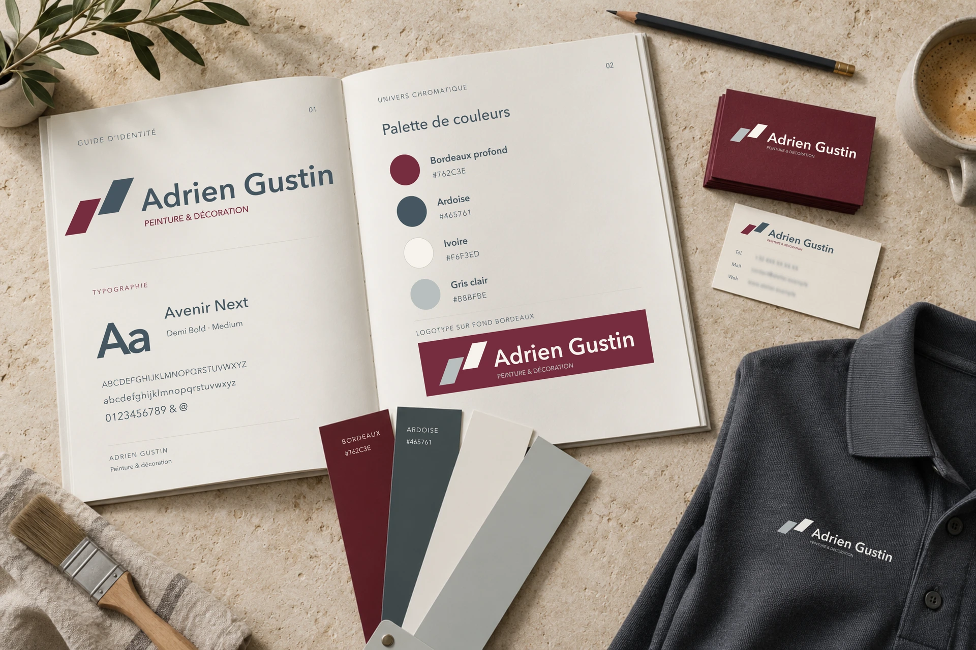 Identité Adrien Gustin présentée sur une table : guide avec logo, palette bordeaux et ardoise, typographie, cartes de visite et polo.